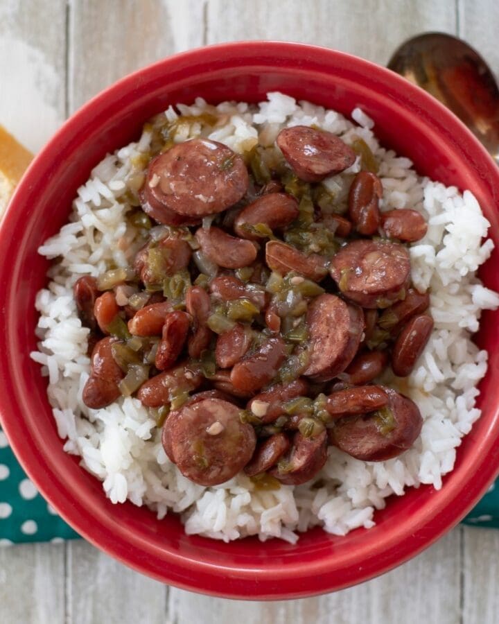 Serving red beans and rice in a red bowl on a teal napkin.