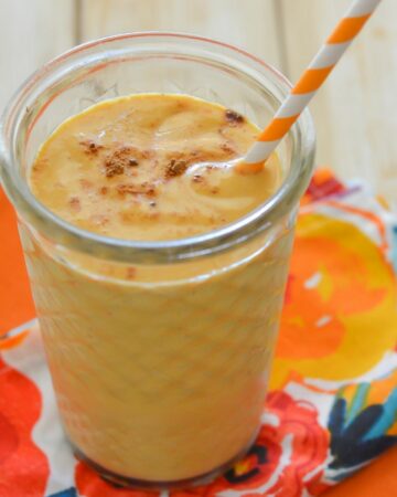 A thick and creamy pumpkin smoothie in a tall glass with a straw.