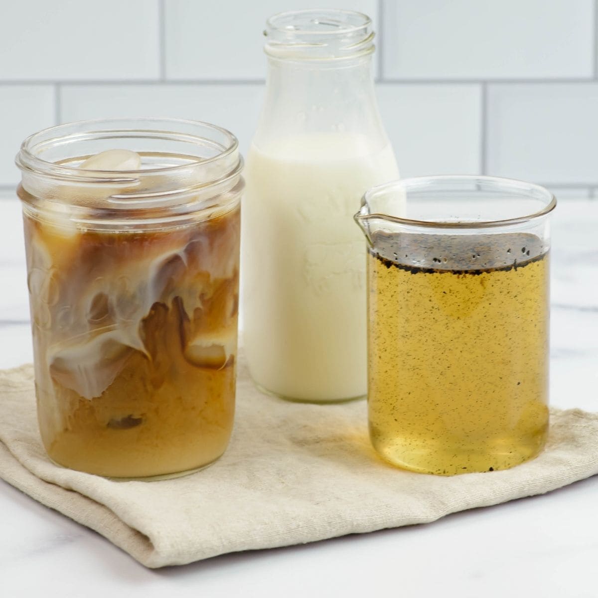 A jar of homemade vanilla coffee syrup next to a bottle of milk and a glass of iced coffee.