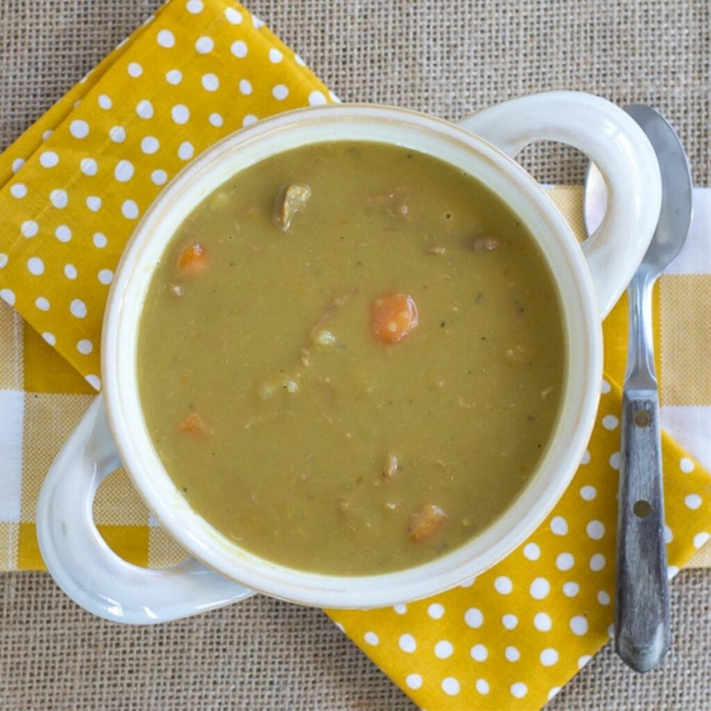 A white soup bowl with handles filled with Split Pea and Ham Soup.