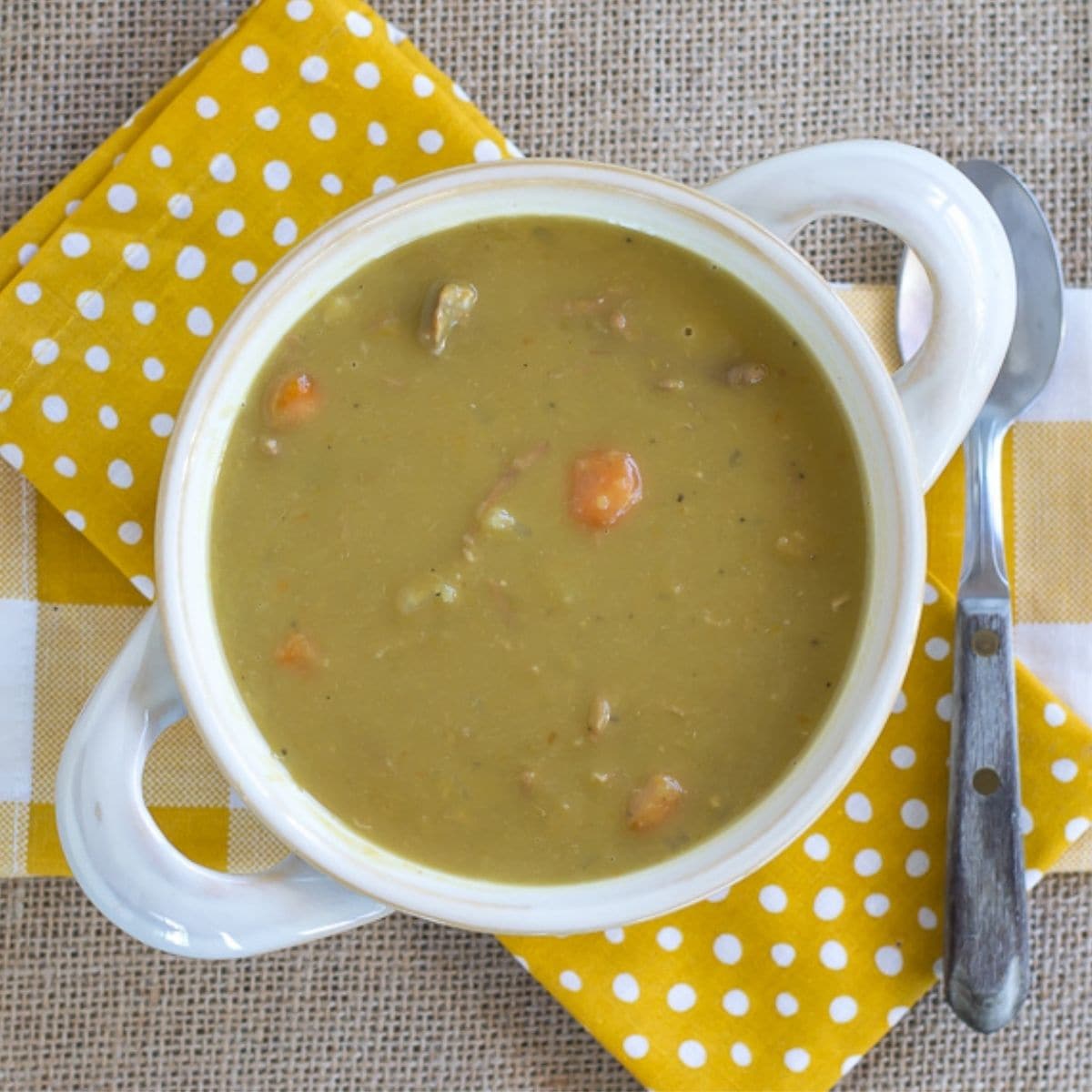 A white soup bowl with handles filled with Split Pea and Ham Soup.