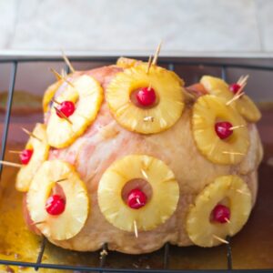 A brown sugar glazed hame with pineapple slices and cherries on a cutting board.