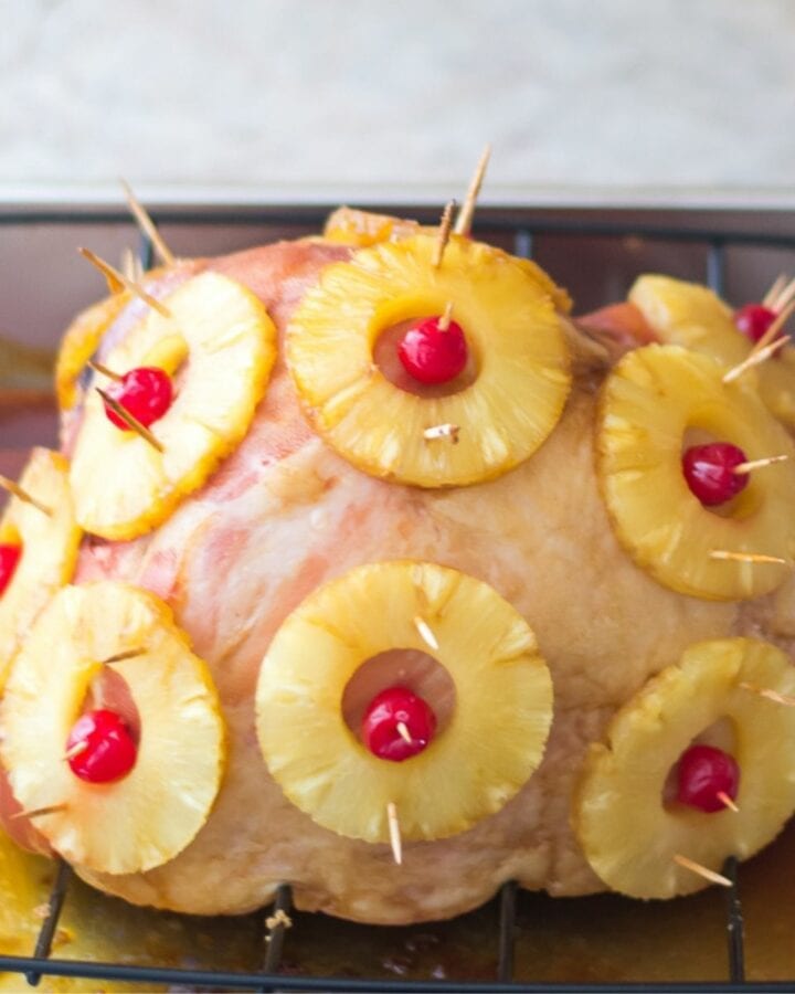 A brown sugar glazed hame with pineapple slices and cherries on a cutting board.