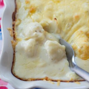 A casserole dish of baked Gouda Cauliflower Casserole with a spoon about to scoop some up.