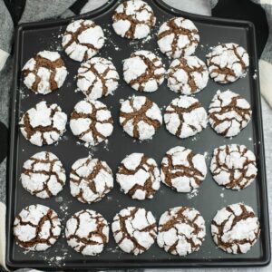 A freshly baked batch of chocolate crinkle cookies arranged on a black serving platter.
