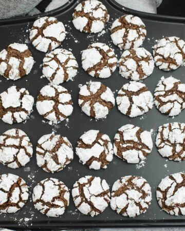 A freshly baked batch of chocolate crinkle cookies arranged on a black serving platter.