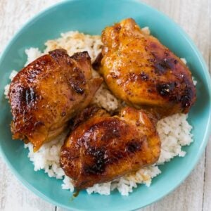 Three browned and glazed chicken thighs in a bowl served over rice.
