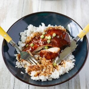 Crock Pot honey garlic chicken breast served on a bed of rice with a green onion garnish.