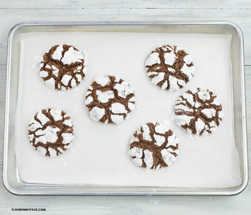 Larger 1 ½ inch chocolate crinkle cookies on a parchment lined  cookie sheet.