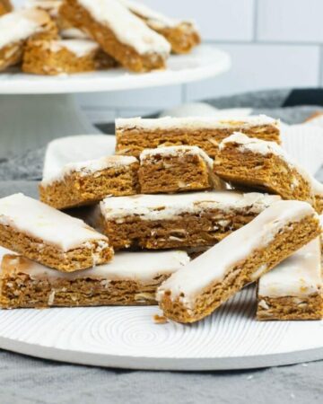 German Honey Bars (Lebkuchen) stacked on a dessert plate with a cake stand in the background with more.