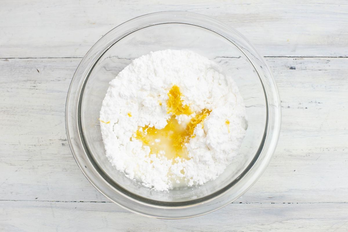 Adding the lemon juice and lemon zest to the bowl of powdered sugar.