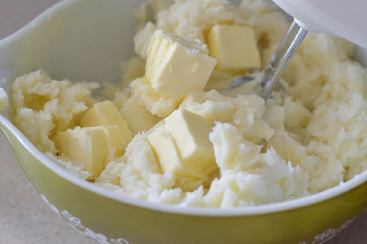 Beating cooked potatoes with butter in a mixing bowl.