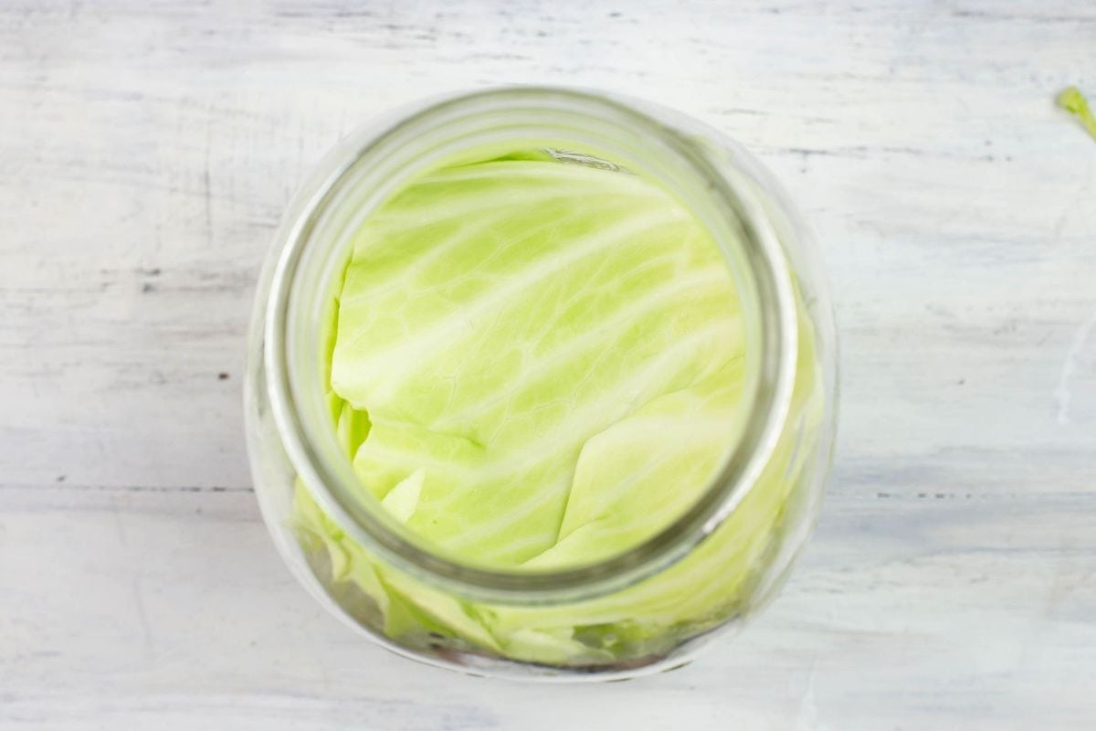 Using a cabbage leaf to cover sauerkraut in a jar.