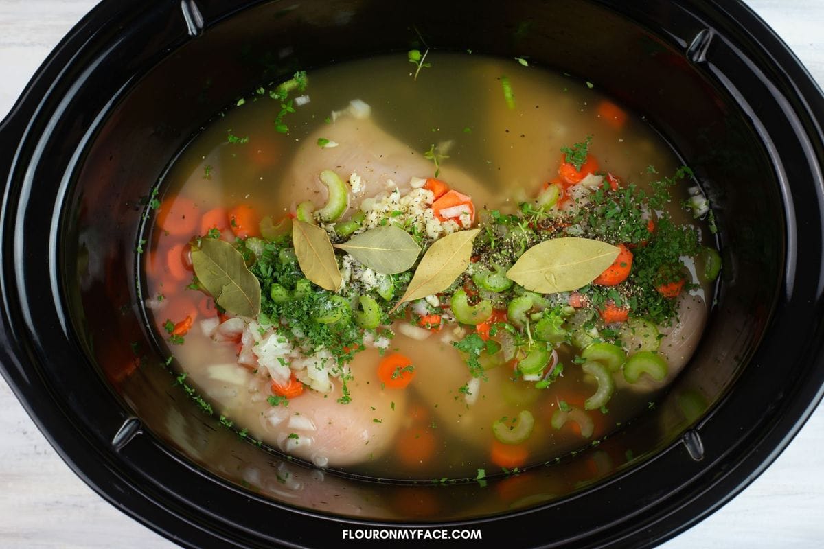 chicken and dumplings ingredients covered in chicken broth in a slow cooker.