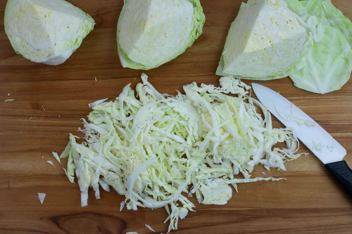Cutting shredded cabbage on a wooden cutting board to make fermented sauerkraut.