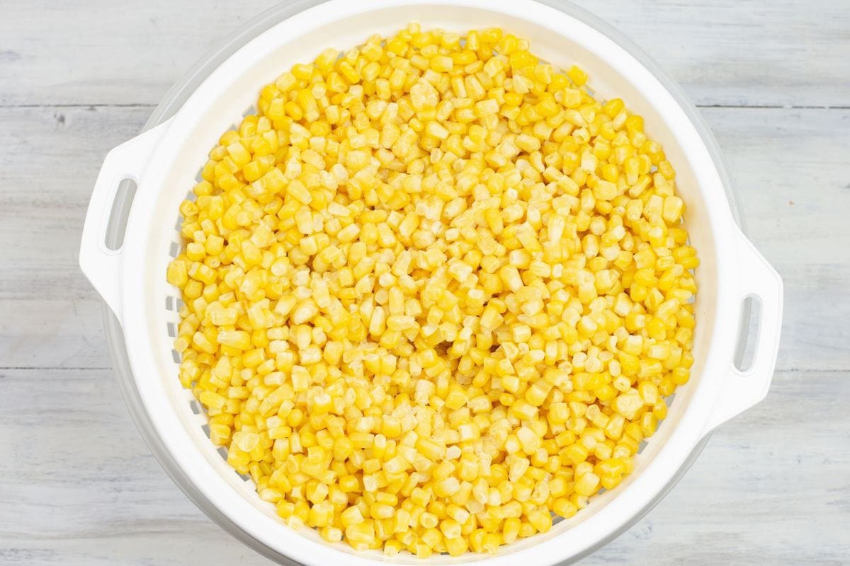 A bag of frozen yellow sweet corn dumped into a colander.