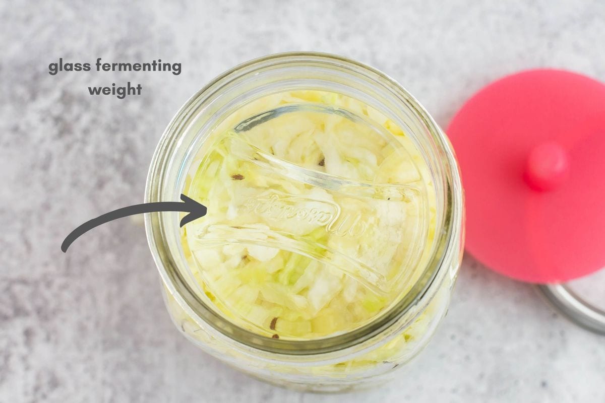 Glass fermenting weight in a jar filled with sauerkraut ingredients.