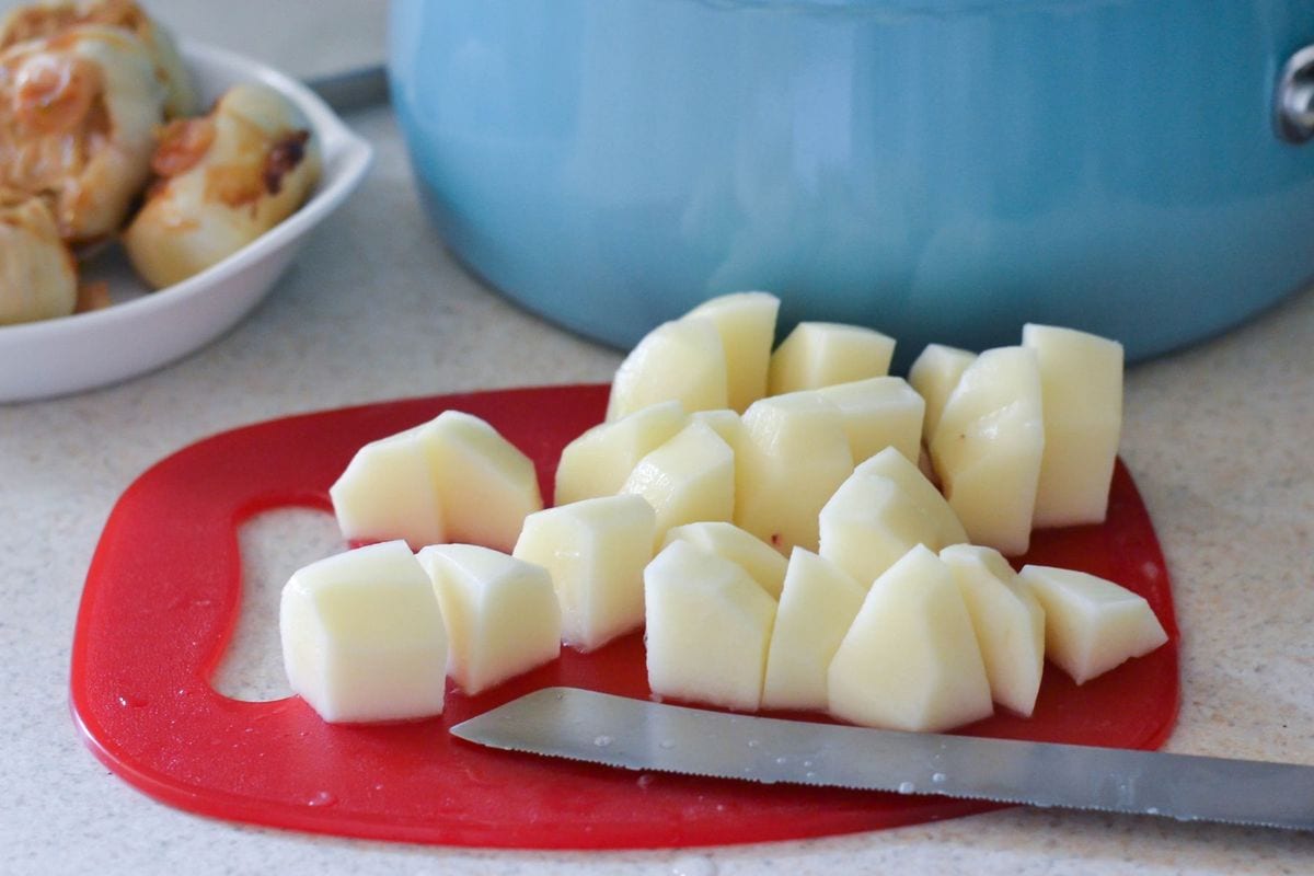 Peeled and quartered potatoes on a red cutting board.