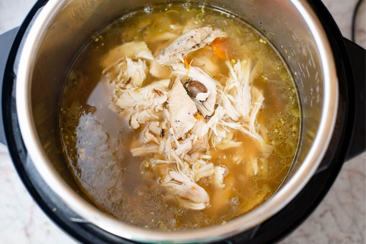 Adding the shredded chicken back to the soup pot.