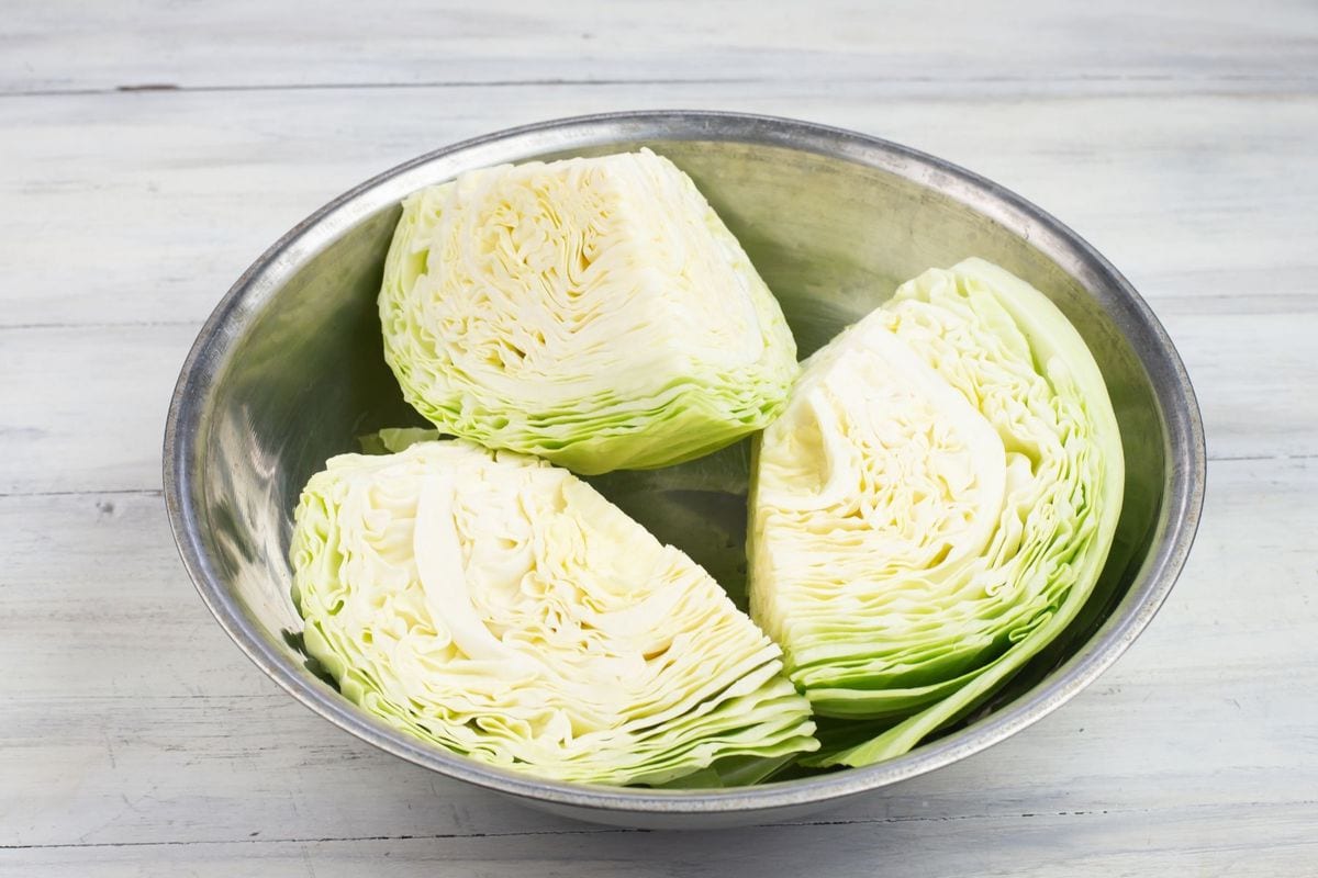A head of fresh cabbage cut into wedges in a bowl.