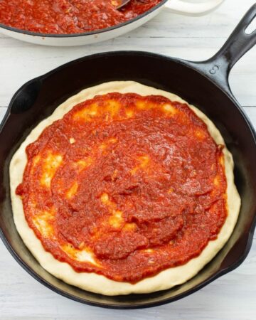 Cast iron skillet pizza dough spread with a thick homemade pizza sauce.