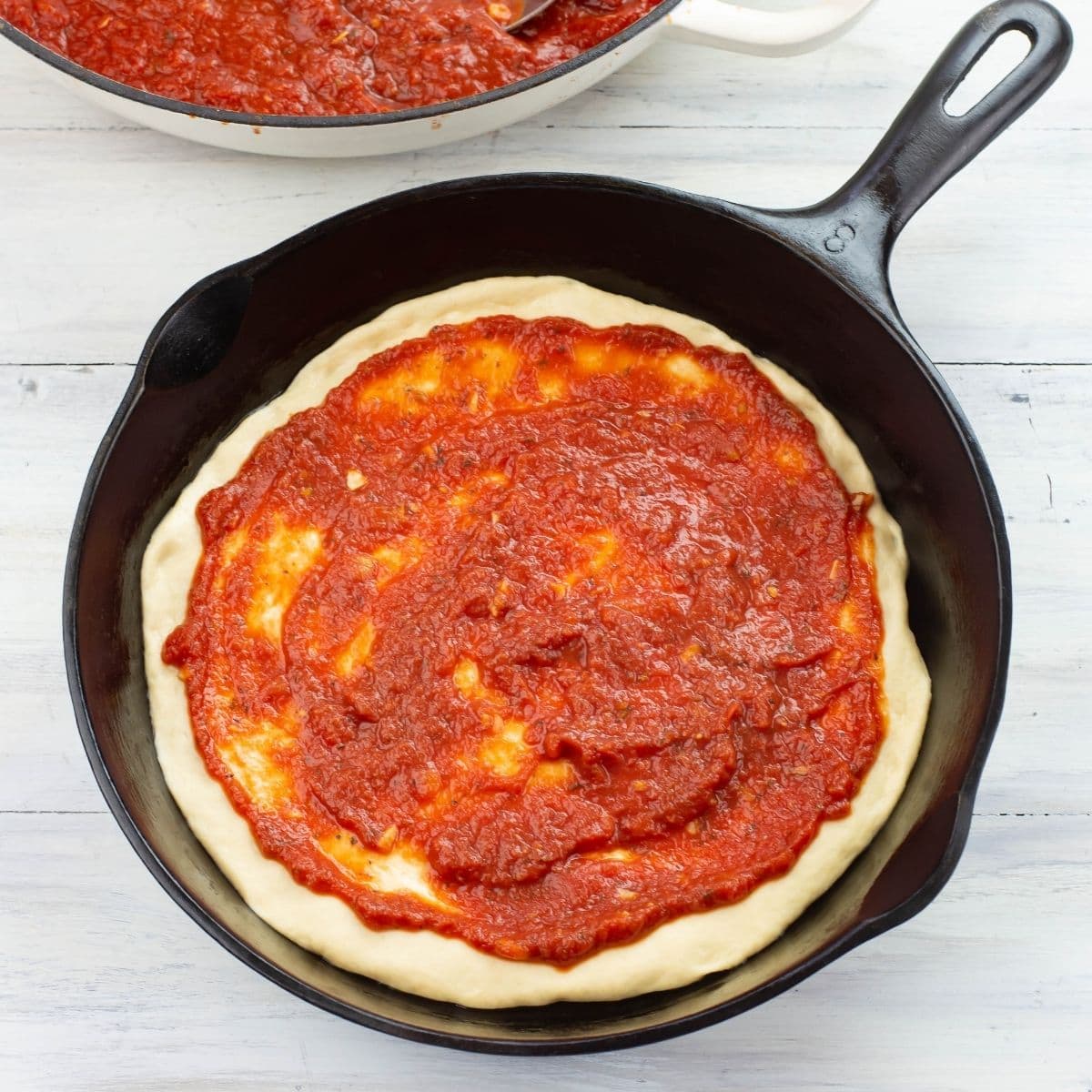 Cast iron skillet pizza dough spread with a thick homemade pizza sauce.