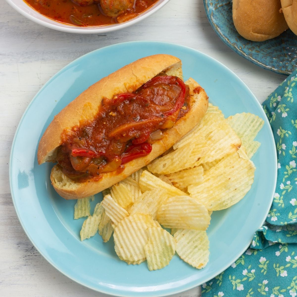 Sausage and peppers cooked in sauce on a bun served with chips.