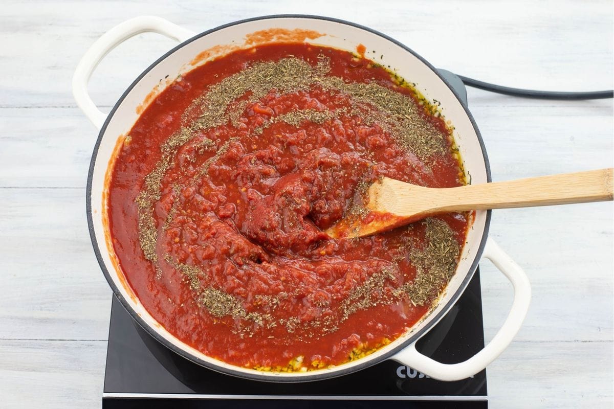 Mixing the seasonings into the sauce with a wooden spoon.