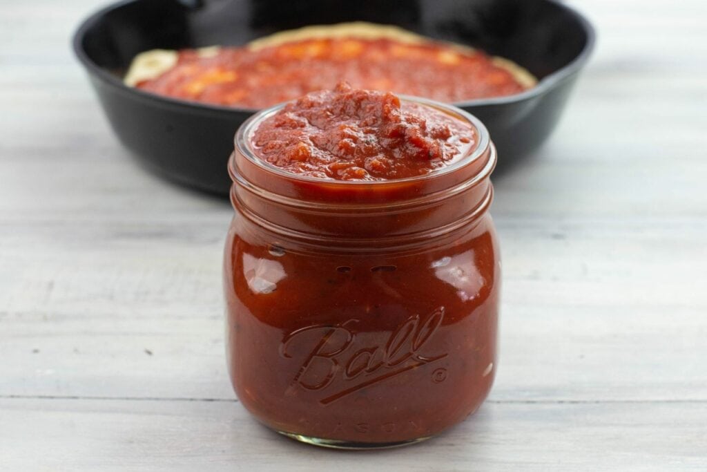 A small glass jar filled to the brim with pizza sauce.