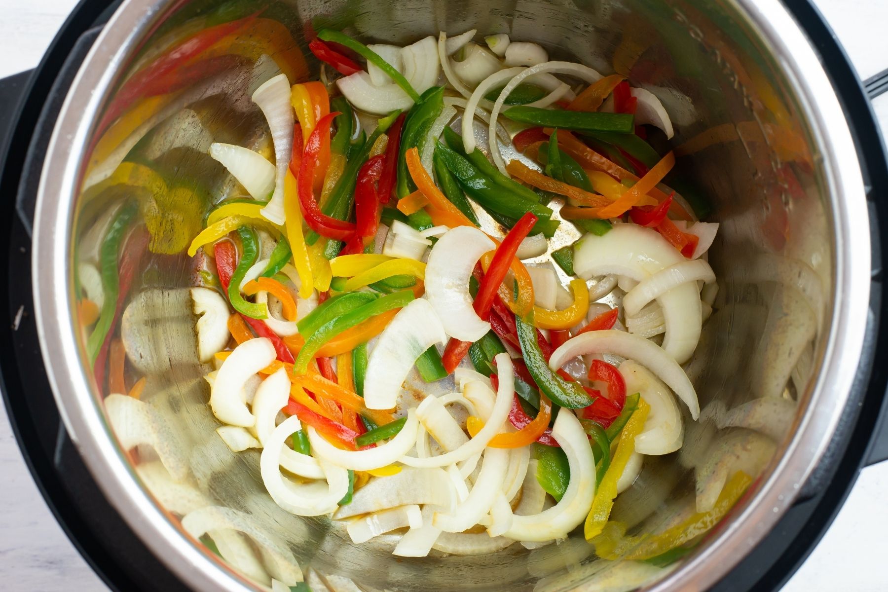 Step 2 adding the sliced peppers and onions to the Instant Pot insert.