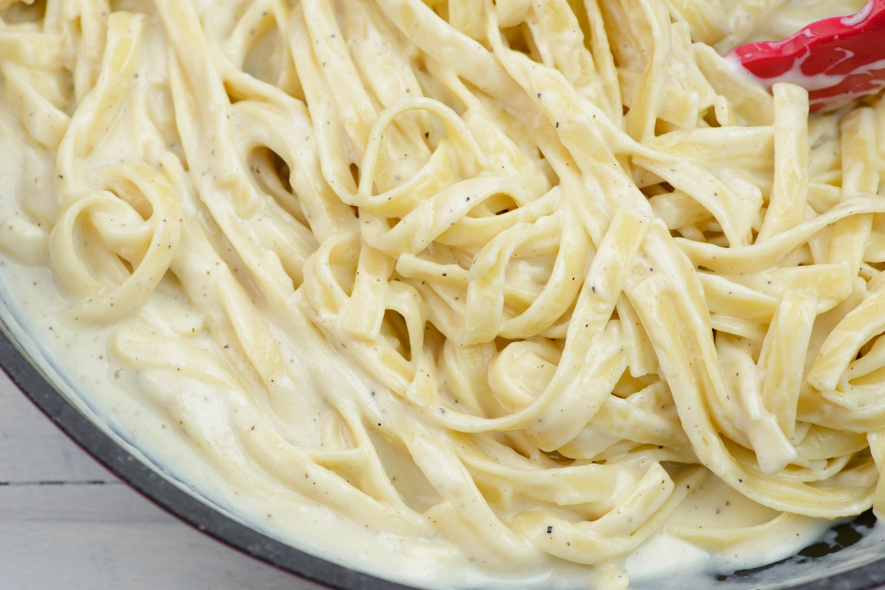 Closeup of fettuccine noodles covered with a thick and creamy alfredo sauce.