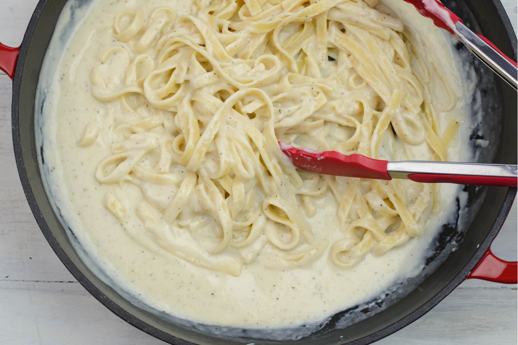 Tossing cooked pasta with alfredo sauce in a red skillet.