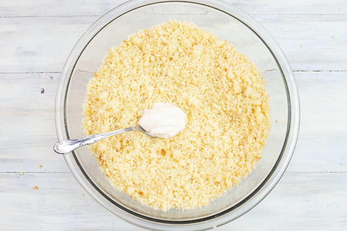 Adding frosting to cake crumbs in a large bowl.