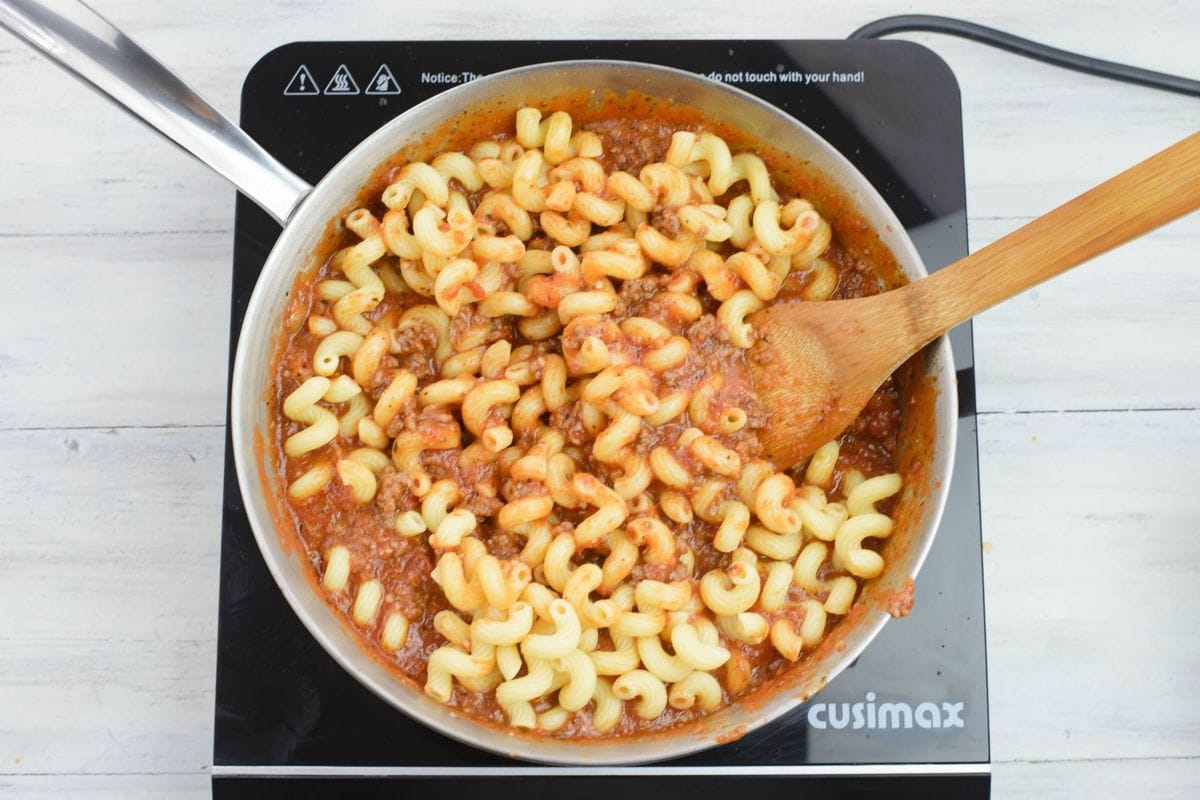Mixing cooked pasta noodles into hot pasta sauce in a pan.