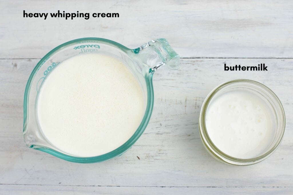 A measuring cup with heavy whipping cream and a small jar filled with buttermilk.