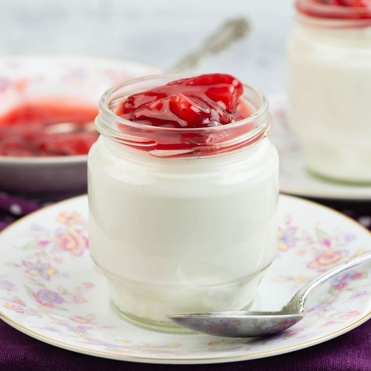 Homemade Vanilla Bean Yogurt in a small jar topped with strawberry preserves.