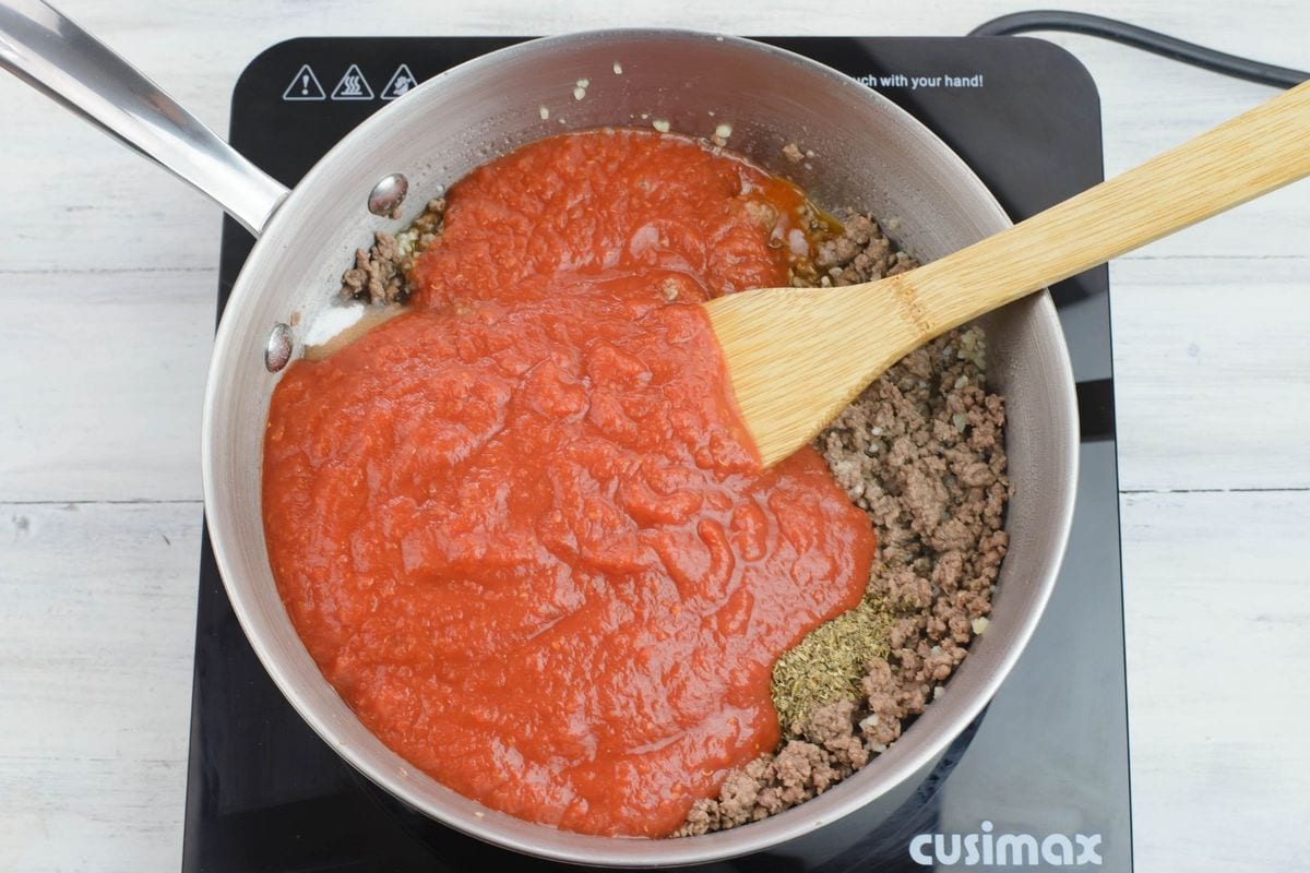 Adding a can of crushed tomatoes to the meat in the pan.