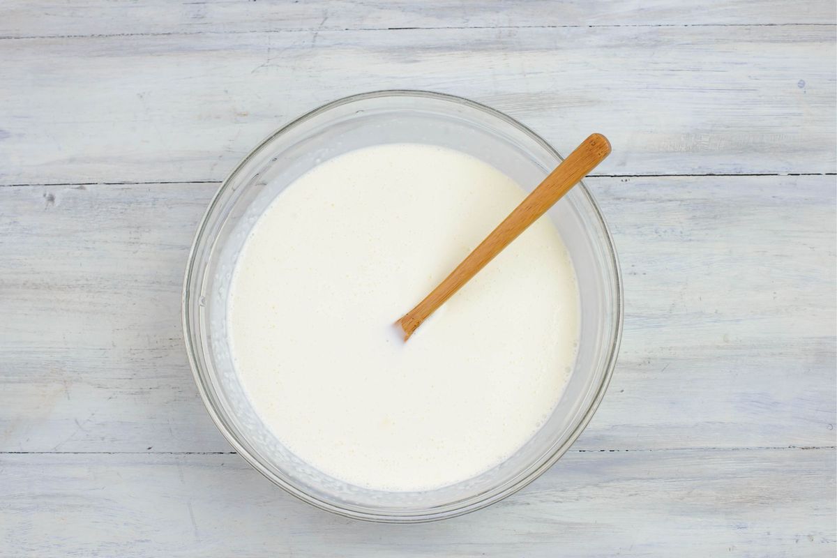 Heavy cream and buttermilk mixed together in a bowl with a spoon.