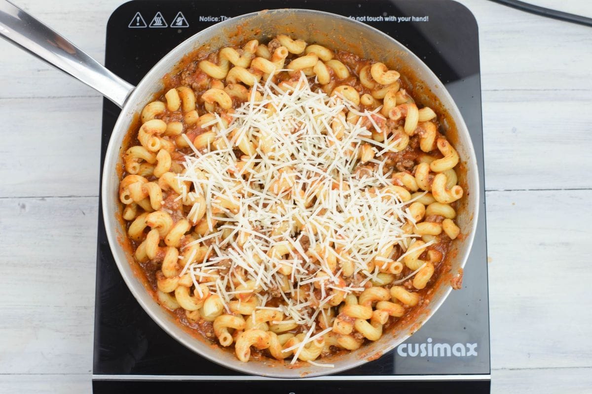 Parmesan cheese topped pasta in a stainless steel skillet.