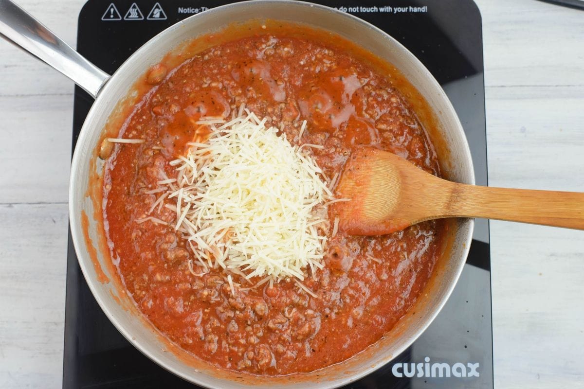 Adding shredded Parmesan cheese to the sauce.