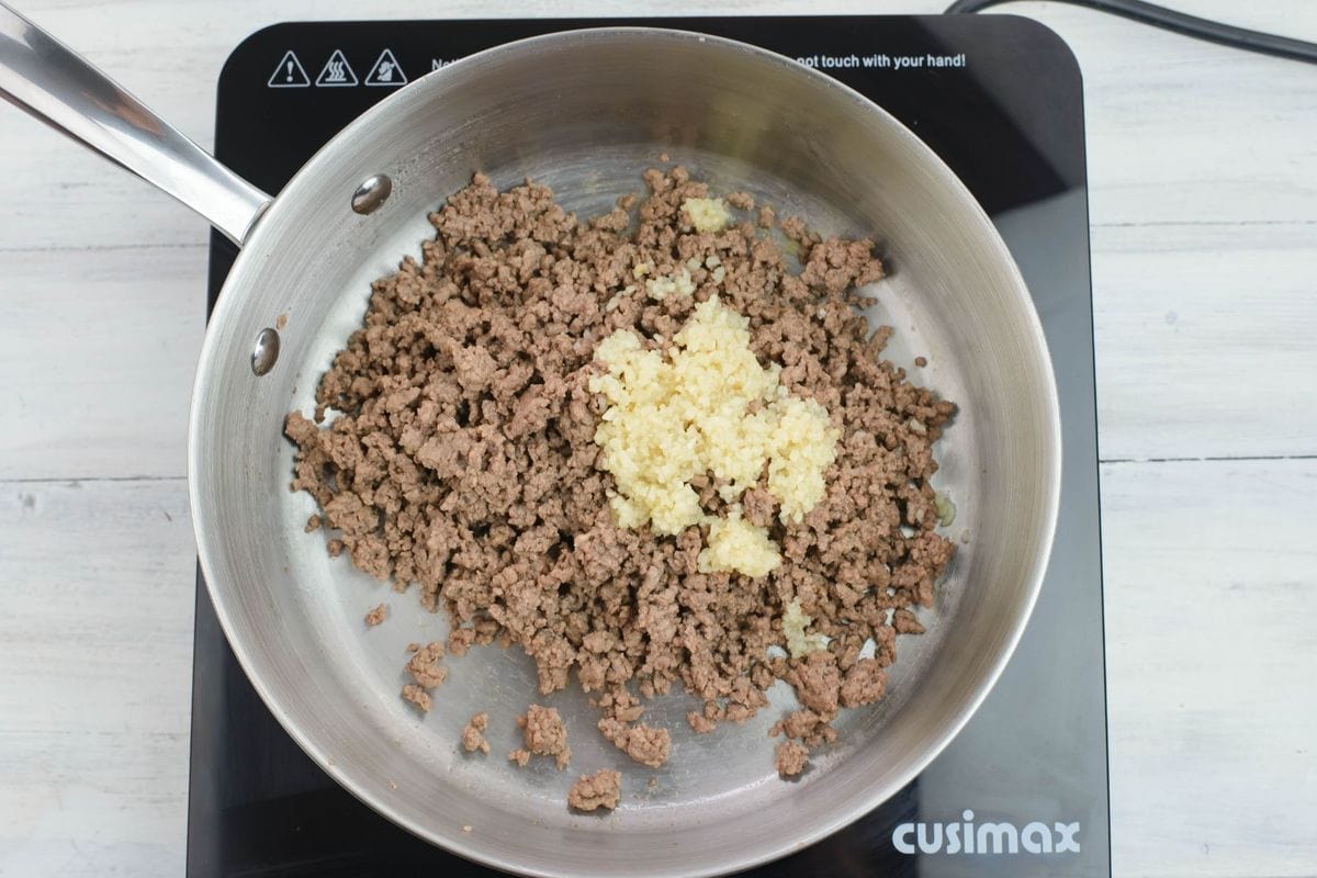 Adding minced garlic to the skillet with ground beef and sautéing until the garlic is soft.