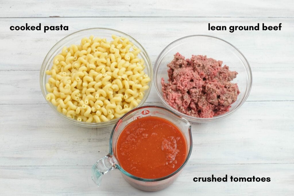 Cooked pasta, raw ground beef and canned crushed tomatoes in individual bowls.