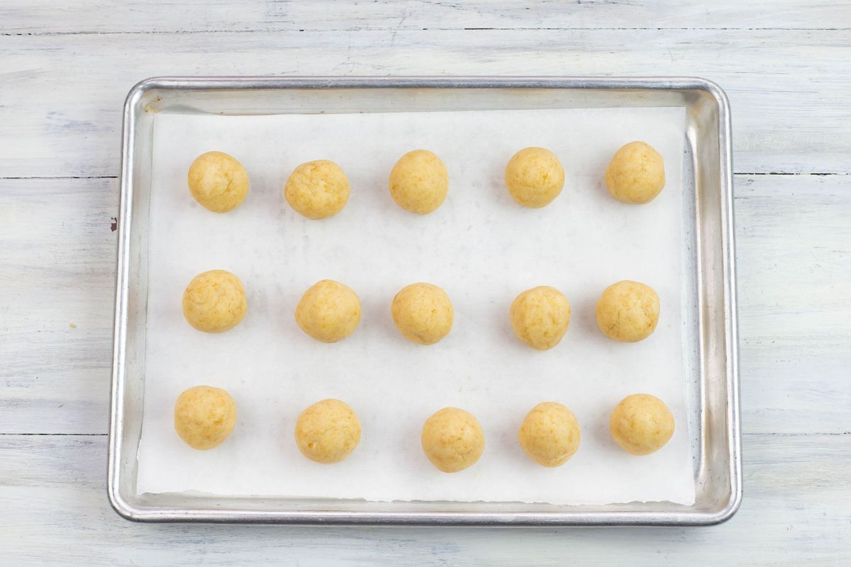 A small baking tray with 15 rolled and shaped cookie balls.