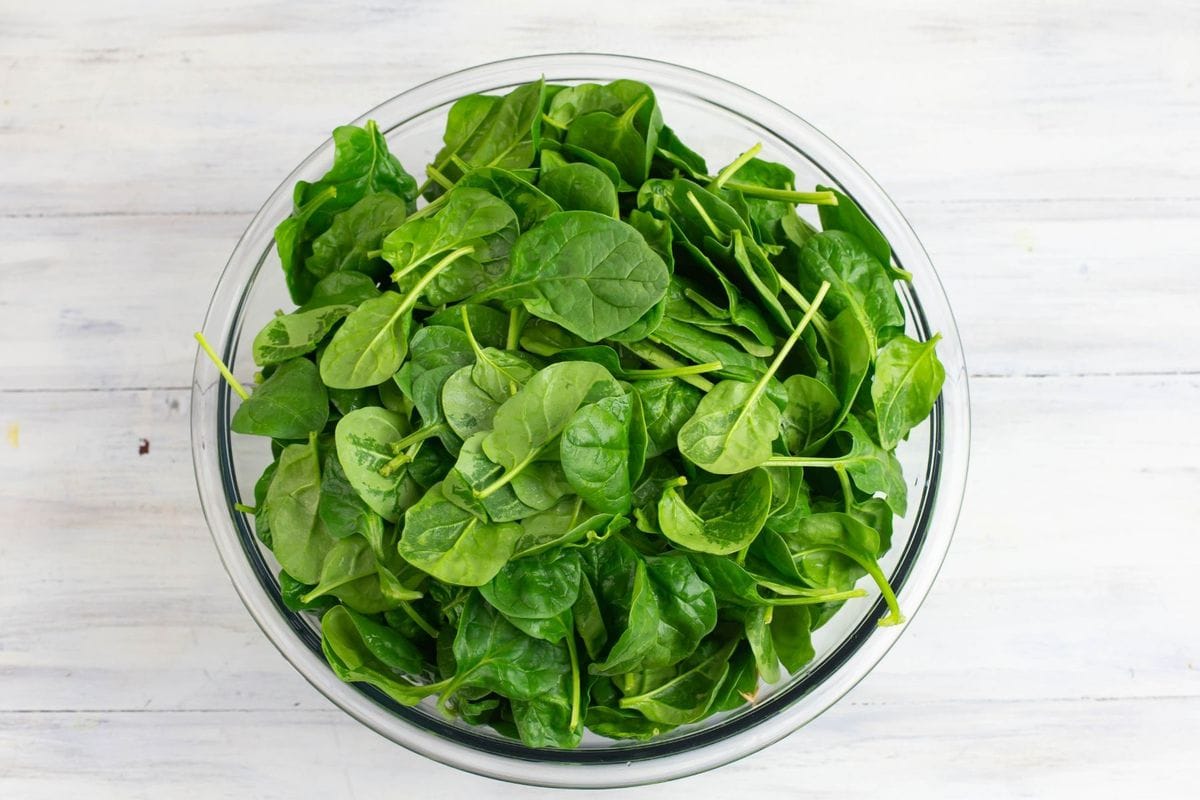 A glass bowl filled with spinach leaves.