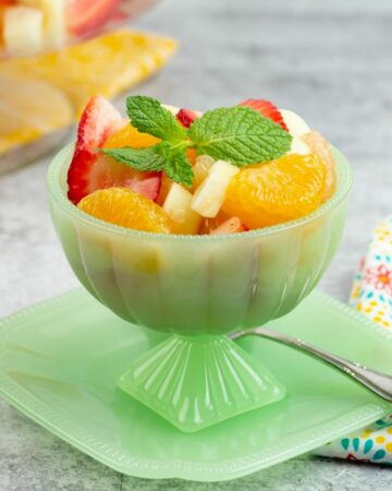 Individual serving bowl filled with citrus fruit salad garnished with a sprig of fresh mint.