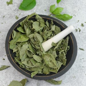 Dry dehydrated basil leaves in a wooden bowl with a pestle before grinding.