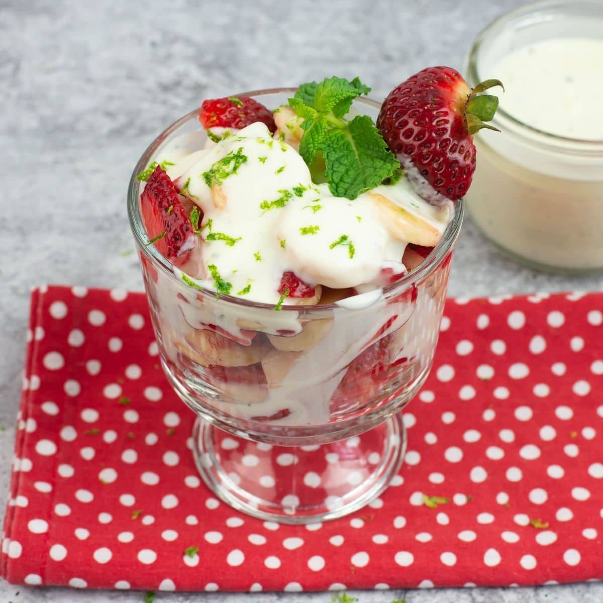 A clear dessert glass filled with fruit drizzled with creamy Yogurt Lime Fruit Salad Dressing.