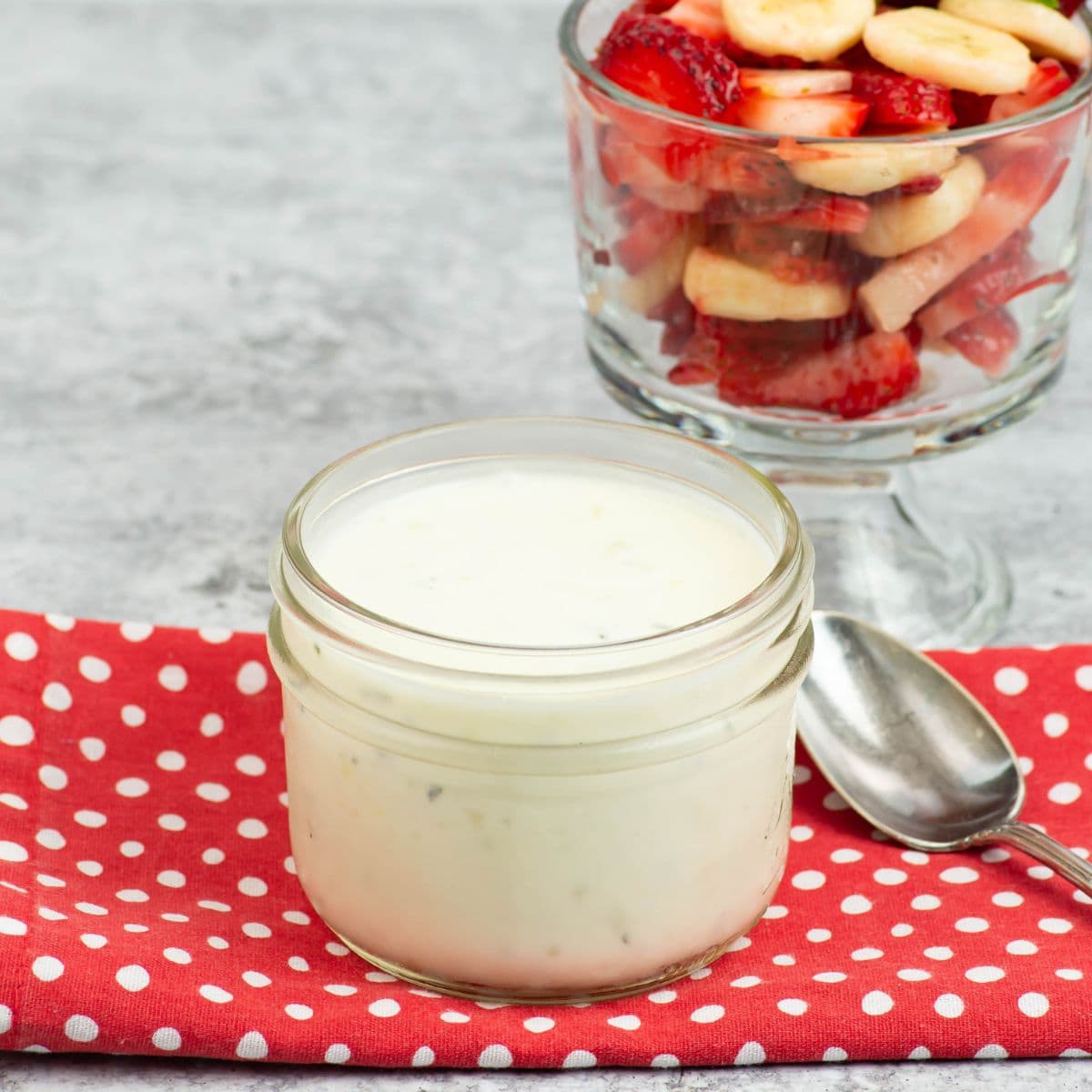 Fruit Yogurt Dressing in a mason jar with a bowl of fruit in the background.