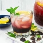 A serving of Hibiscus lemonade in a glass with lemon slice and mint sprig garnish.
