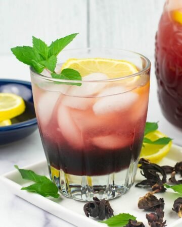 A serving of Hibiscus lemonade in a glass with lemon slice and mint sprig garnish.